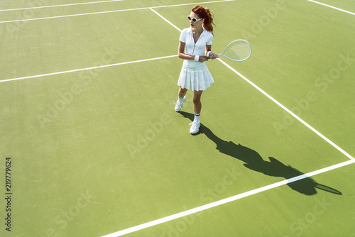 side view of young attractive woman in white tennis uniform playing tennis on court