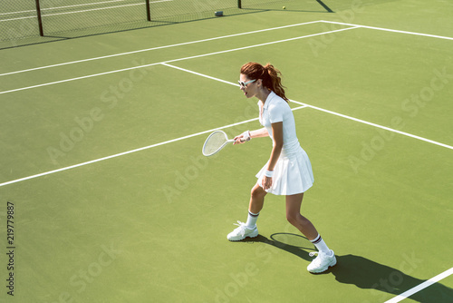 young female tennis player in sunglasses playing tennis on court