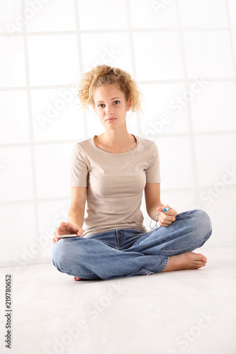 sitting young woman thoughtful with earphones and cell phone, long hair and dressed in jeans and T shirt isolated on white room background on floor