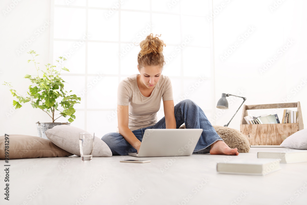 young woman with computer, smartphone and books, sitting on the floor in living room on white wide window in the background young woman with computer, smartphone and books, sitting on the floor in living room on white wide window in the background