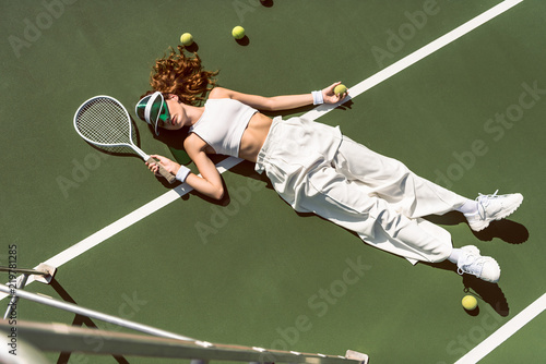 high angle view of stylish woman in white clothing and cap lying with racket lying on tennis court with racket © LIGHTFIELD STUDIOS
