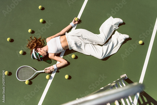 overhead view of attractive woman in white clothing and cap lying with racket lying on tennis court with racket © LIGHTFIELD STUDIOS