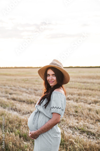 lovely pregnant woman next to the hay bale in the sunlight