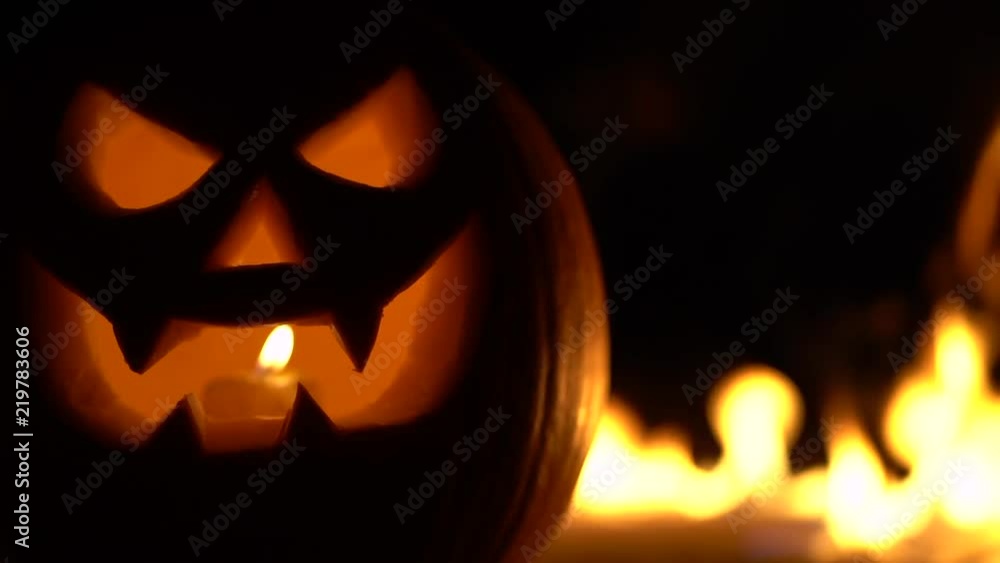 Dreadful mad pumpkin as head of Jack-o-lantern with carved eyes and wicked smirk on burning hell fire. Scary symbol of Halloween, All Hallows' Eve. Gourd on left side. Slow motion. Dreadful mad pumpkin as head of Jack-o-lantern with carved eyes and wicked smirk on burning hell fire. Scary symbol of Halloween, All Hallows' Eve. Gourd on left side. Slow motion.