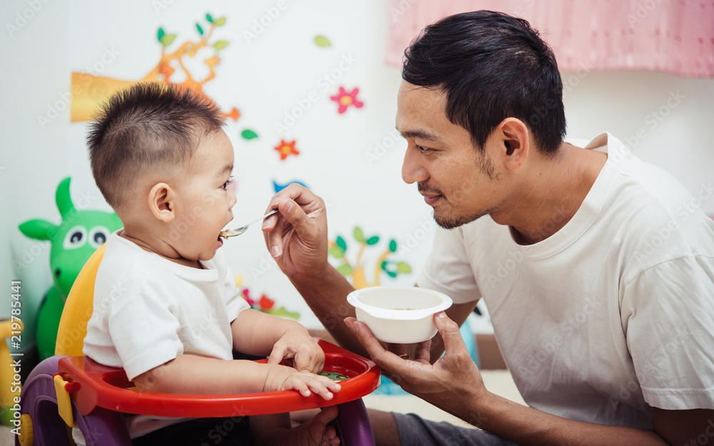 Father acting Mom feeding his son baby 1 year old on chair