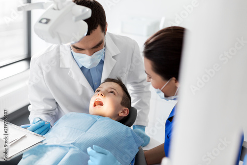 medicine  dentistry and healthcare concept - dentist with mouth mirror checking for kid patient teeth at dental clinic
