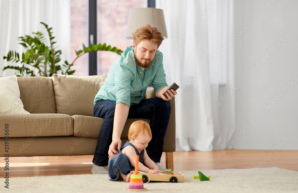 family, fatherhood and people concept - happy red haired father with smartphone and little baby daughter playing with toy blocks kit at home family, fatherhood and people concept - happy red haired father with smartphone and little baby daughter playing with toy blocks kit at home