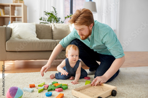family, fatherhood and people concept - happy red haired father and little baby daughter playing with toy blocks kit at home