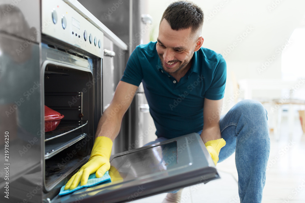 household and people concept - man wiping table with cloth cleaning oven door at home kitchen household and people concept - man wiping table with cloth cleaning oven door at home kitchen