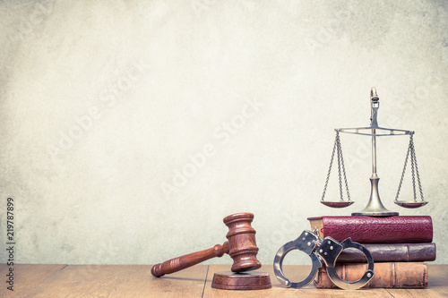 Wooden gavel, Vintage law scales, handcuffs and books on the desk front concrete wall background. Symbols of justice still life. Retro old style filtered photo