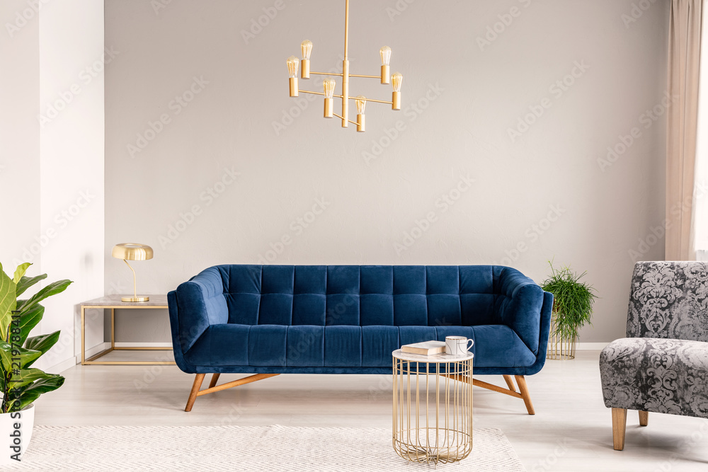 Gold lamp hanging above royal blue sofa in real photo of light grey sitting  room interior with empty wall Stock Photo | Adobe Stock