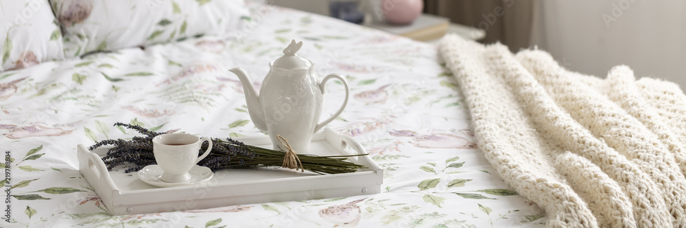 Real photo of white tray with tea cup, porcelain jug and fresh lavender placed on floral bedding on bed with knit blanket Real photo of white tray with tea cup, porcelain jug and fresh lavender placed on floral bedding on bed with knit blanket