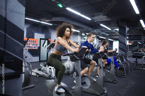 Young people doing exercises on elliptical trainer in gym photo