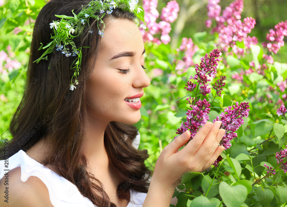 Beautiful young woman wearing flower wreath near blossoming shrub on sunny spring day Beautiful young woman wearing flower wreath near blossoming shrub on sunny spring day