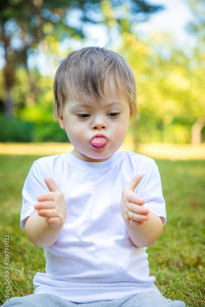 Portrait of Cute small boy with Down syndrome playing in summer day on nature Portrait of Cute small boy with Down syndrome playing in summer day on nature