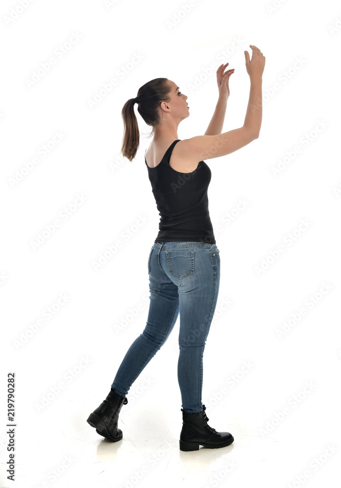 full length portrait of brunette girl wearing black single and jeans. standing pose in side profile. isolated on white studio background. full length portrait of brunette girl wearing black single and jeans. standing pose in side profile. isolated on white studio background.