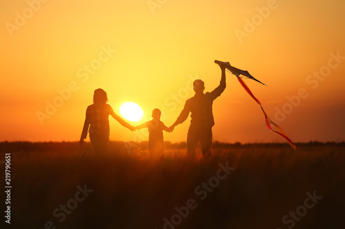 Happy family flying kite in the field at sunset