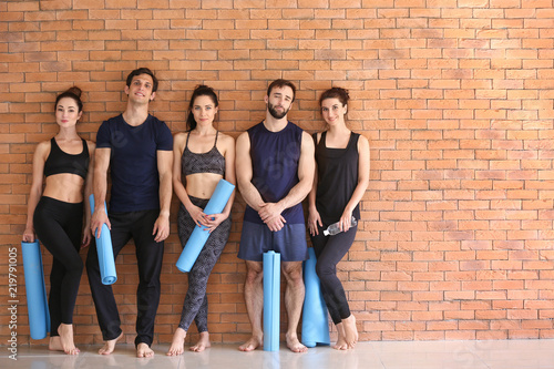 Group of people with yoga mats near brick wall