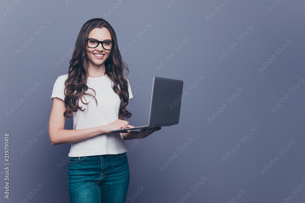 Adorable attractive smart clever lovely stylish nice cute cheerful curly-haired brunette girl in casual white t-shirt, jeans and glasses, holding opened laptop, copy-space, isolated on grey background Adorable attractive smart clever lovely stylish nice cute cheerful curly-haired brunette girl in casual white t-shirt, jeans and glasses, holding opened laptop, copy-space, isolated on grey background