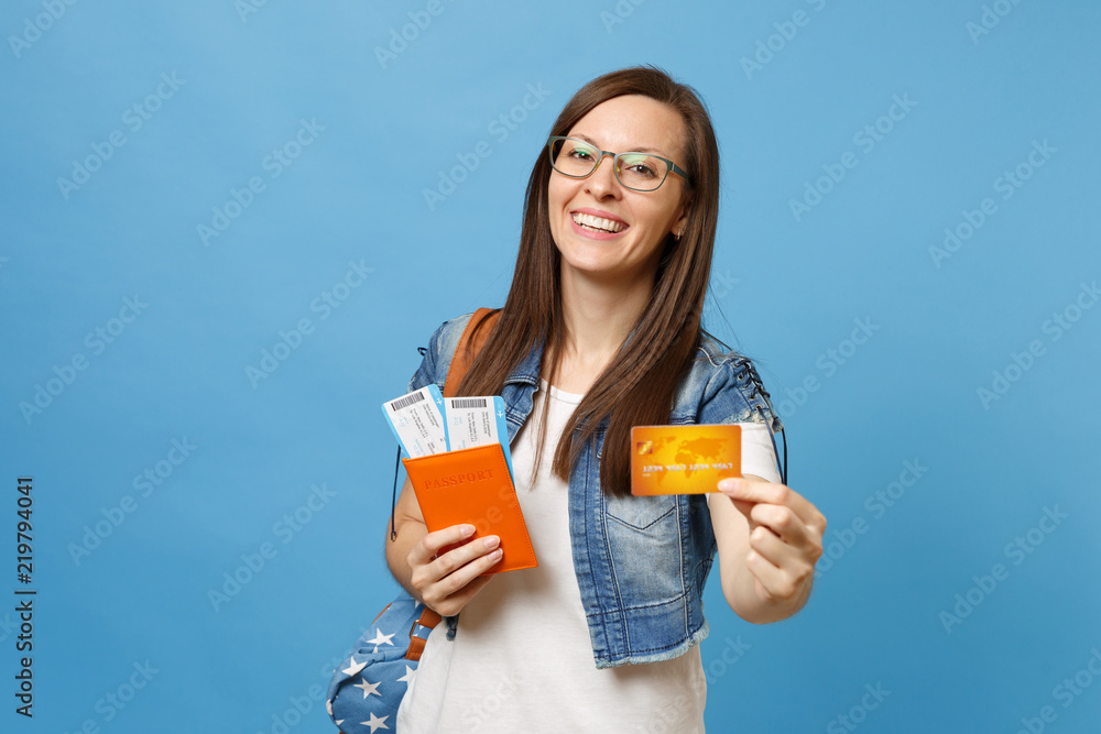 Young laughing woman student in glasses with backpack holding passport boarding pass tickets credit card isolated on blue background. Education in university college abroad. Air travel flight concept. Young laughing woman student in glasses with backpack holding passport boarding pass tickets credit card isolated on blue background. Education in university college abroad. Air travel flight concept.
