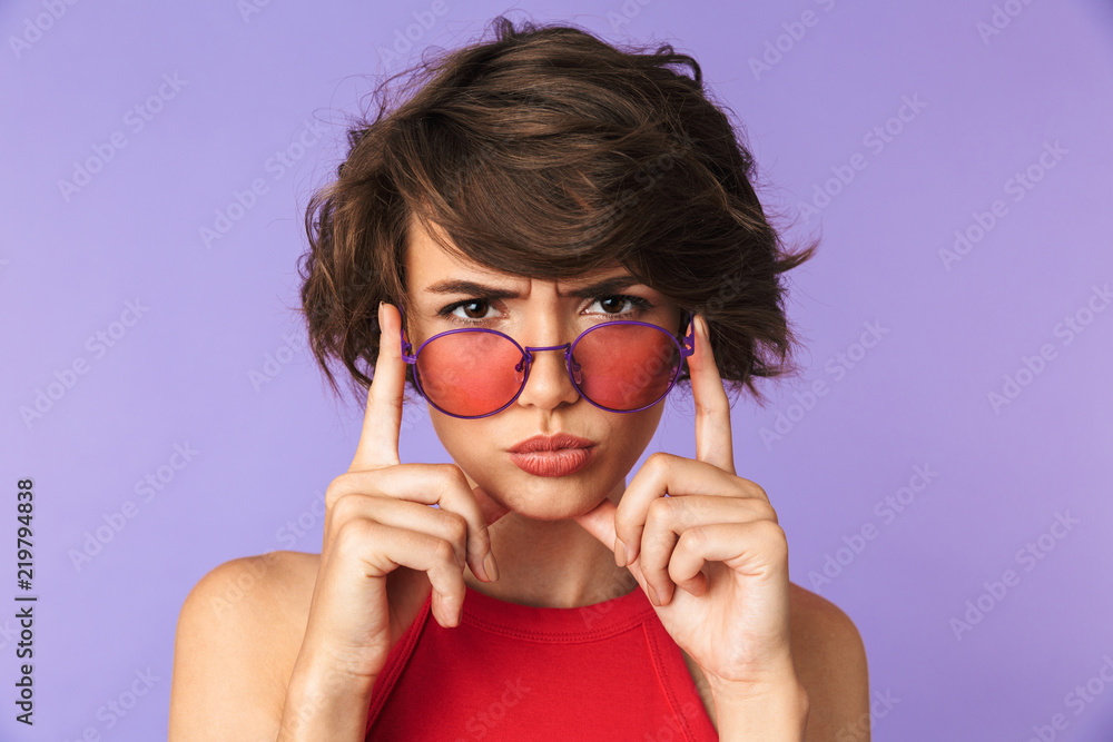 Serious Pretty brunette woman in sunglasses looking at the camera Serious Pretty brunette woman in sunglasses looking at the camera