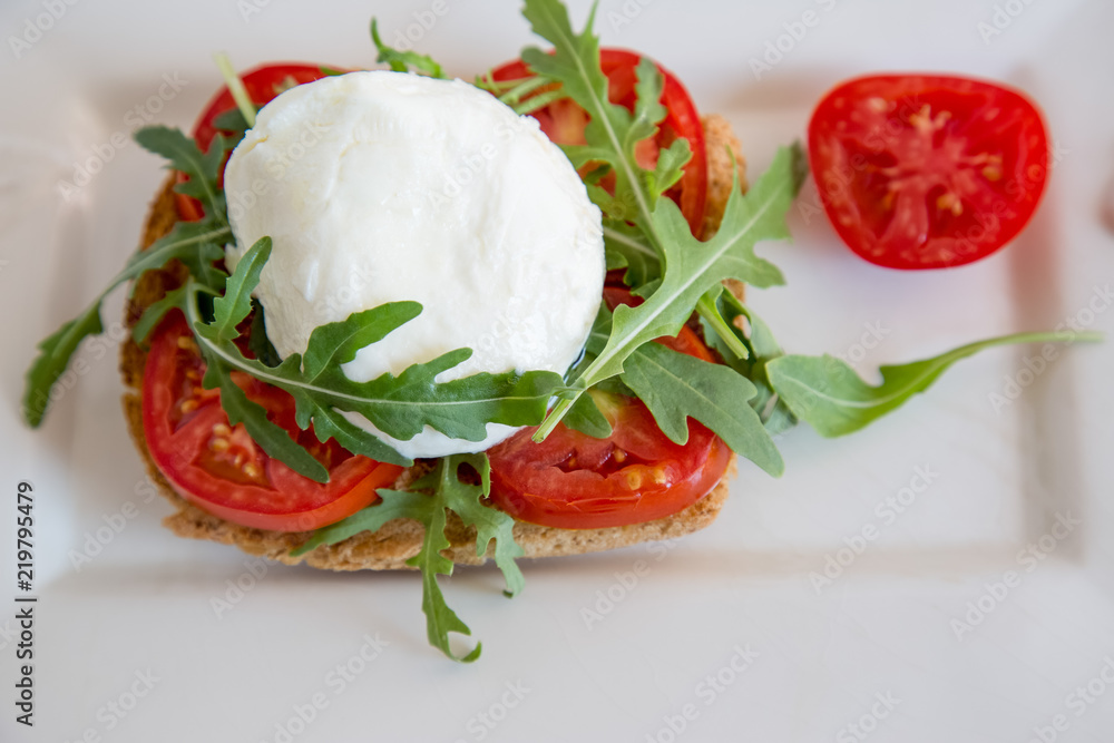 Italian style toast with light bread, arugula, tomato and mozzarella cheese Italian style toast with light bread, arugula, tomato and mozzarella cheese
