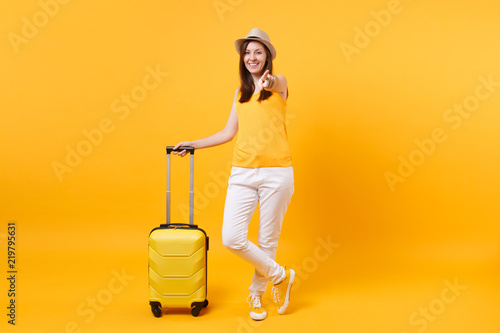 Traveler tourist woman in summer casual clothes, hat with suitcase isolated on yellow orange background. Female passenger traveling abroad to travel on weekends getaway. Air flight journey concept.