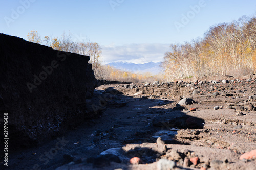 Road after mudflow. A lot of huge stones and dirt are everywhere. Blue sky and trees are around. Russia Autumn 2017 Kamchatka.