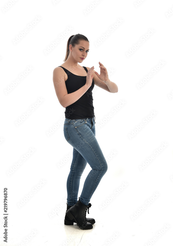 full length portrait of brunette girl wearing black single and jeans. standing pose in side profile. isolated on white studio background. full length portrait of brunette girl wearing black single and jeans. standing pose in side profile. isolated on white studio background.