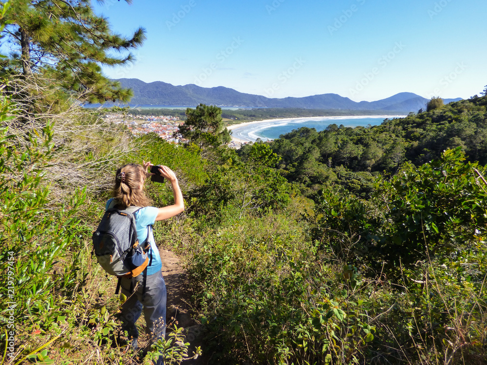 Woman taking a picture of Mocambique beach viewed from Boa vista hiking path - Florianopolis, Brazil