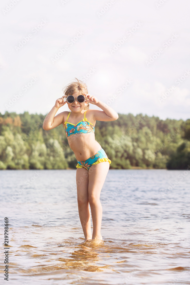 a small blonde girl with a tail in a swimsuit and glasses fooling