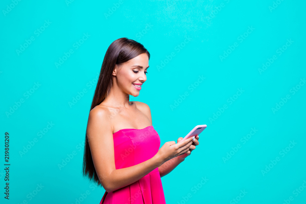 Young straight-haired sweet tender brunette smiling girl with long hair, opened mouth, wearing pink top, writing sms in phone. Copy space. Isolated over bright vivid turquoise background Young straight-haired sweet tender brunette smiling girl with long hair, opened mouth, wearing pink top, writing sms in phone. Copy space. Isolated over bright vivid turquoise background
