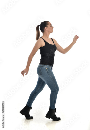  full length portrait of brunette girl wearing black single and jeans. standing pose in side profile. isolated on white studio background.