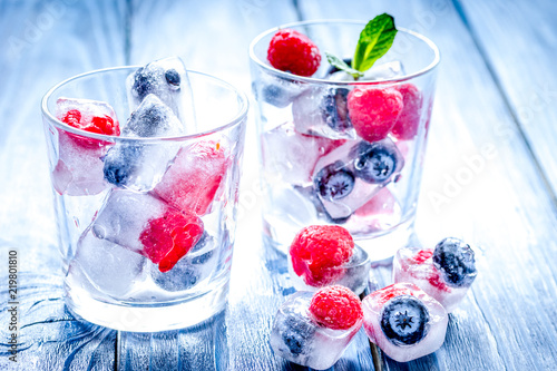 Ice cubes with blueberry and raspberry in glass on wooden table
