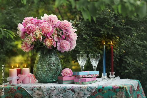 A bouquet of romantic pink peonies in a glass vase. Dinner by candlelight in the garden.