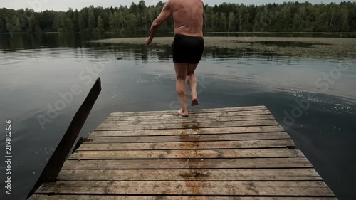 Caucasian mature man jumping from wooden pier in lake. Having fun in vacation in country side.