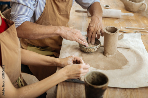 Earthenware items. Strong mature man wearing striped shirt making earthenware items along with his wife