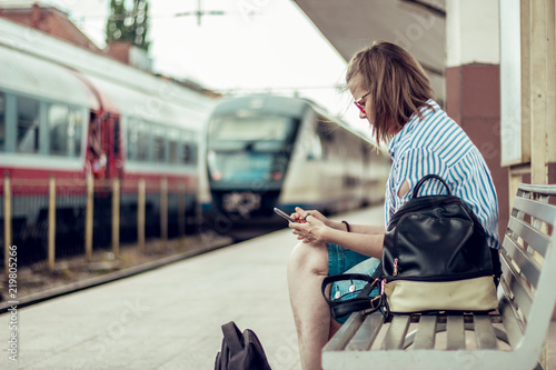 Girl using a mobile phone in a train station. Young woman sitting texing on a smartphone photo