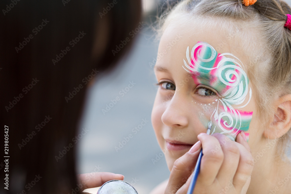 Fototapeta premium Little girl getting her face painted by face painting artist.