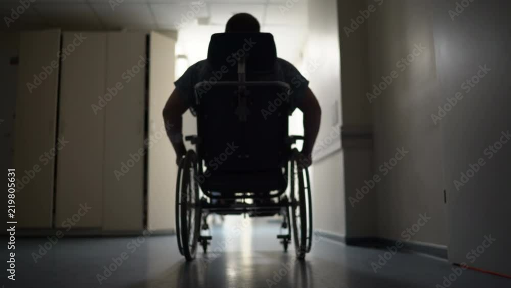 Silhouette of disabled man on wheelchair moving down hospital hallway Silhouette of disabled man on wheelchair moving down hospital hallway