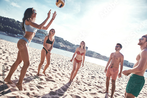 Time with friends. Group of young people playing volleyball on the beach