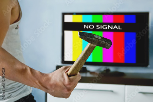 viewer is furious with the problems with broadcasting. Multi-colored stripes on the TV screen. The inscription on the TV NO SIGNAL. televiewer wants to smash the monitor with a hammer
