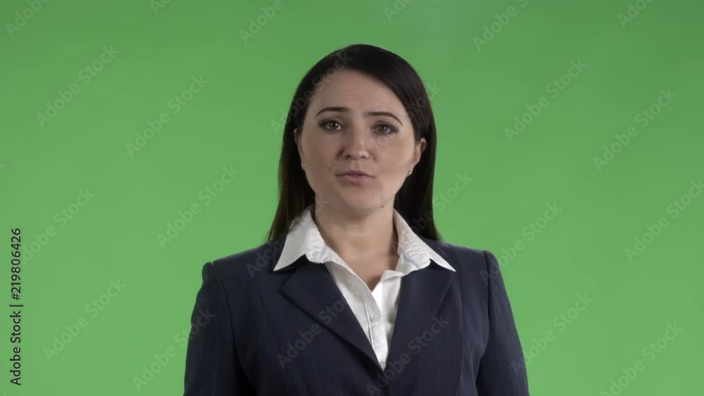 Woman in dark business suit talking to camera against a green screen Woman in dark business suit talking to camera against a green screen