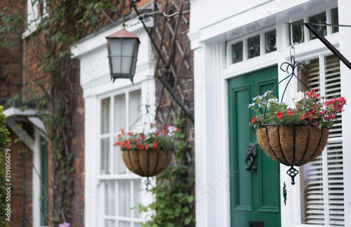 Beautiful traditional house front: flower baskets, a lantern, an entrance door, a window, a brick wall. Concept: English lifestyle and gardening.