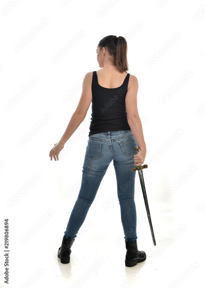 full length portrait of brunette girl wearing black single and jeans. standing pose holding a sword. isolated on white studio background. full length portrait of brunette girl wearing black single and jeans. standing pose holding a sword. isolated on white studio background.