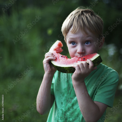 cute little boy eating watermelon on the grass