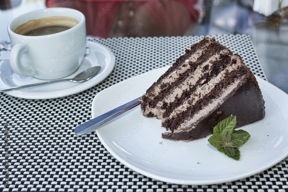 A piece of cake in chocolate glaze sideways and mint leaves. Dark layers alternate with light A piece of cake in chocolate glaze sideways and mint leaves. Dark layers alternate with light