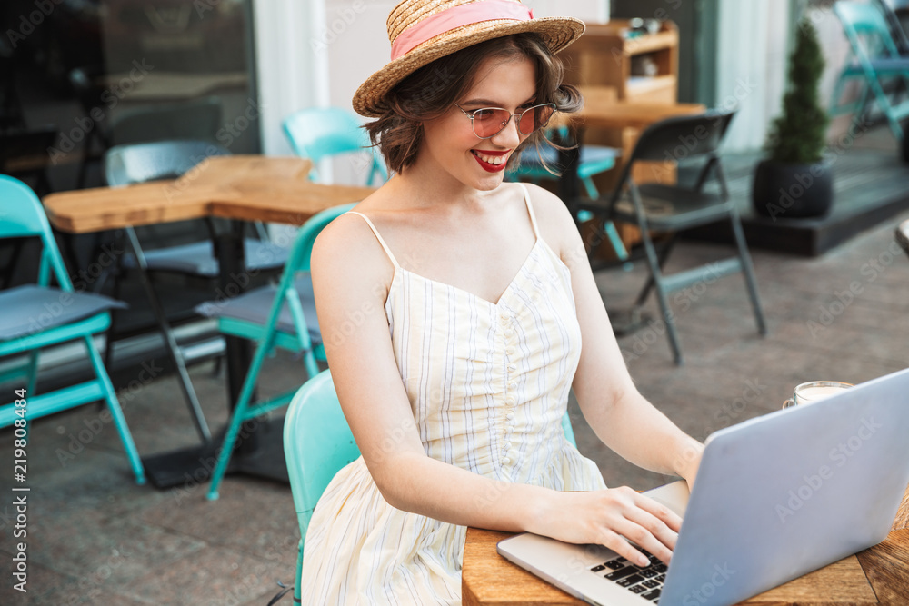 Happy woman in dress and straw hat using laptop computer