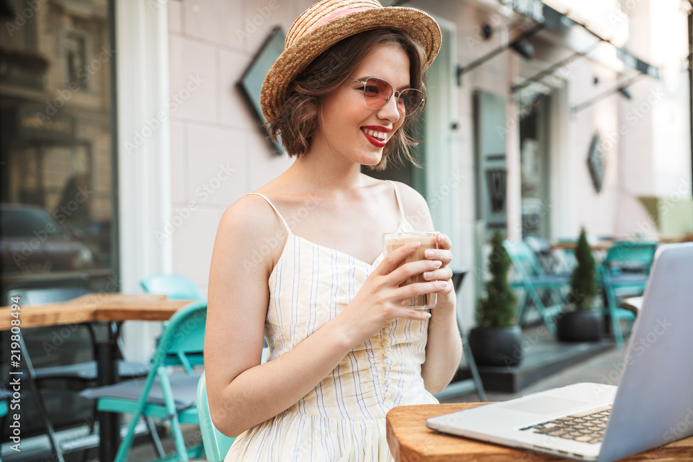 Happy woman in dress and straw hat drinking coffee