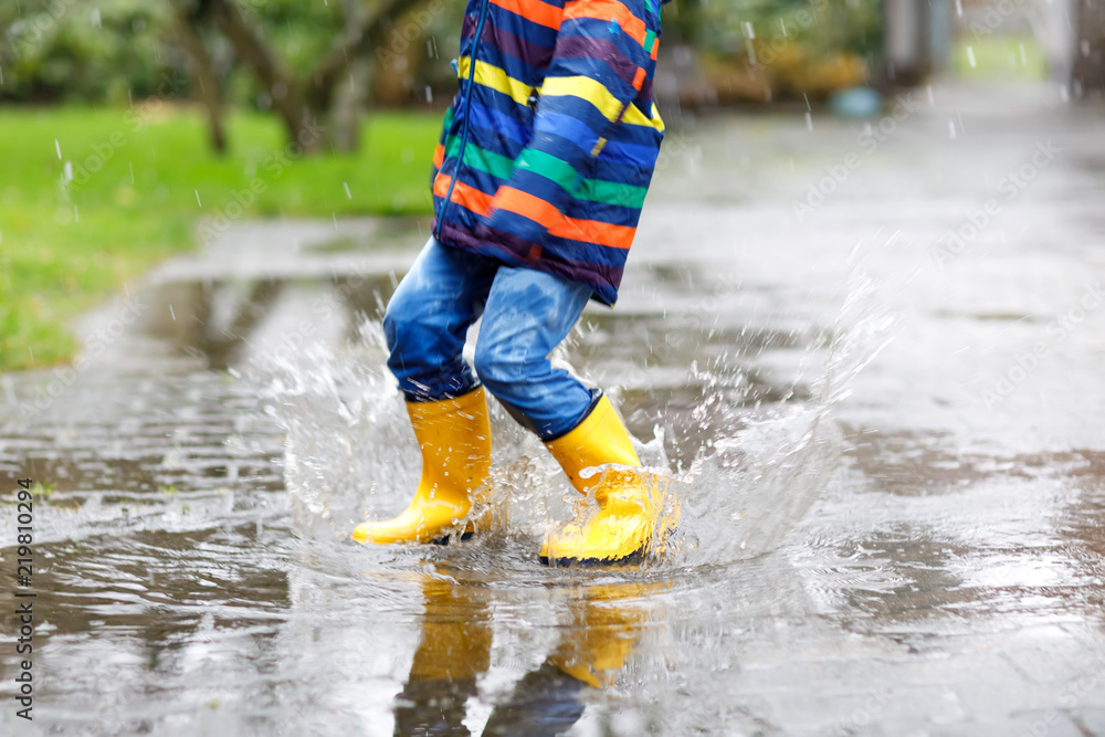 Close-up of kid wearing yellow rain boots and walking during sleet, rain and snow on cold day. Child in colorful fashion casual clothes jumping in a puddle. Having fun outdoors Close-up of kid wearing yellow rain boots and walking during sleet, rain and snow on cold day. Child in colorful fashion casual clothes jumping in a puddle. Having fun outdoors